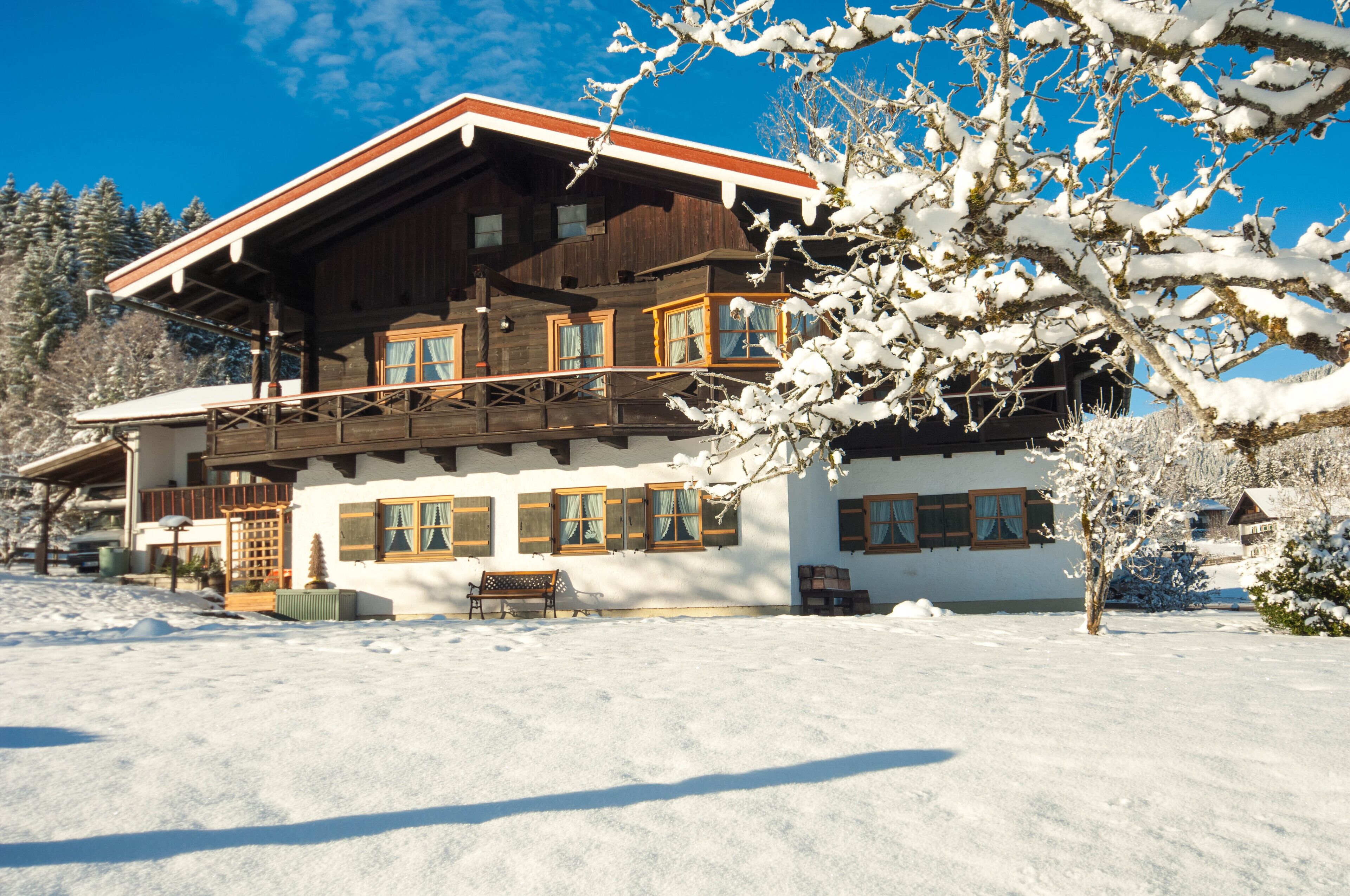 A large wooden chalet with multiple windows and balconies, surrounded by snow-covered trees.