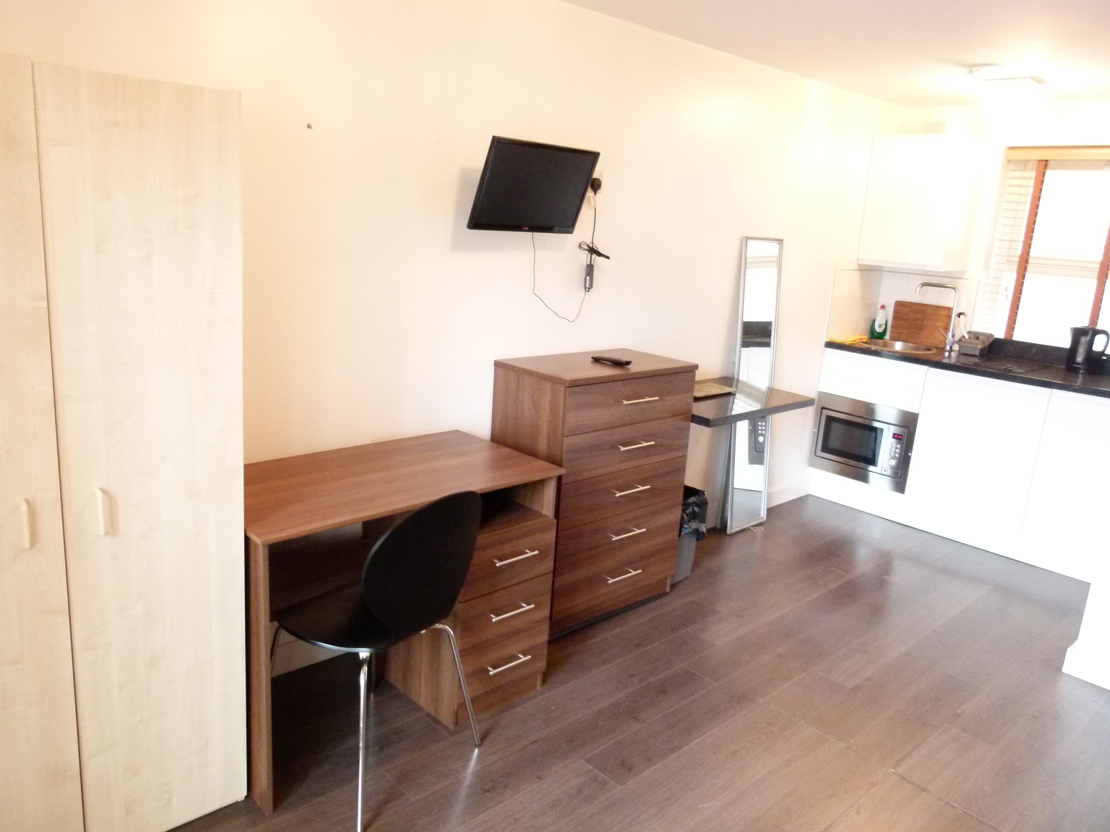 Une petite cuisine équipée d’un bureau en bois, d’une chaise, d’un téléviseur à écran plat fixé au mur et d’un four à micro-ondes.