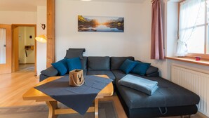 A modern living room with a sofa, a wooden table, and a painting of a landscape. - Ferienwohnung III° extra Schlafzimmer, Süd-Balkon, 65 qm° (Aschau im Chiemgau)
