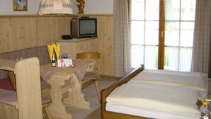 A wooden room with a bed, a table, a chair, a television, and a window with curtains. - Vacation apartment Ramsau for 2 persons, 1 bed-sitting room, terrace, 28 sqm (Inzell)