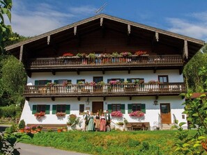 A two-story building with balconies adorned with flowers, a wooden roof, and a white facade. - Apartment Kranzhorn 2 persons, 46 sqm, 1 bedroom (Flintsbach am Inn)