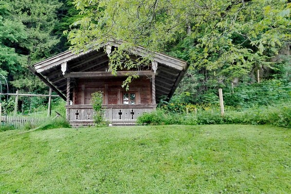 A rustic wooden cabin with a sloped roof, surrounded by lush greenery and trees. - Apartment Kranzhorn 2 persons, 46 sqm, 1 bedroom (Flintsbach am Inn)