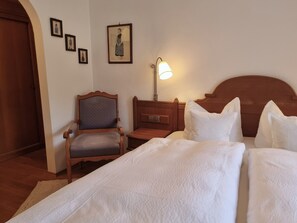 Habitación de hotel con cama, una silla, mesita de noche, lámpara y cuadros en la pared.