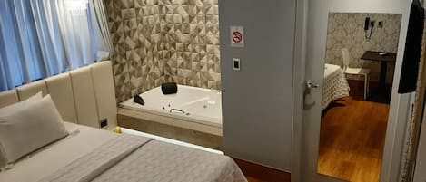 Habitación de hotel con cama, baño con ducha y puerta con letrero de prohibido fumar.