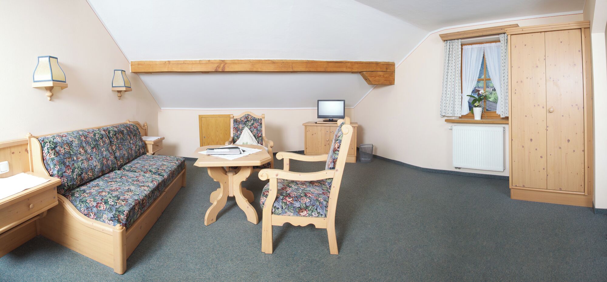 A cozy room with a wooden bed, a small desk, a chair, a table, and a TV.