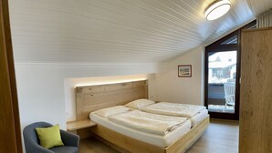 A bedroom with a wooden bed, a nightstand, a chair, and a view of the outside.
