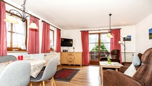 Un salon chaleureux avec un coin repas, des meubles en bois et un téléviseur fixé au mur.