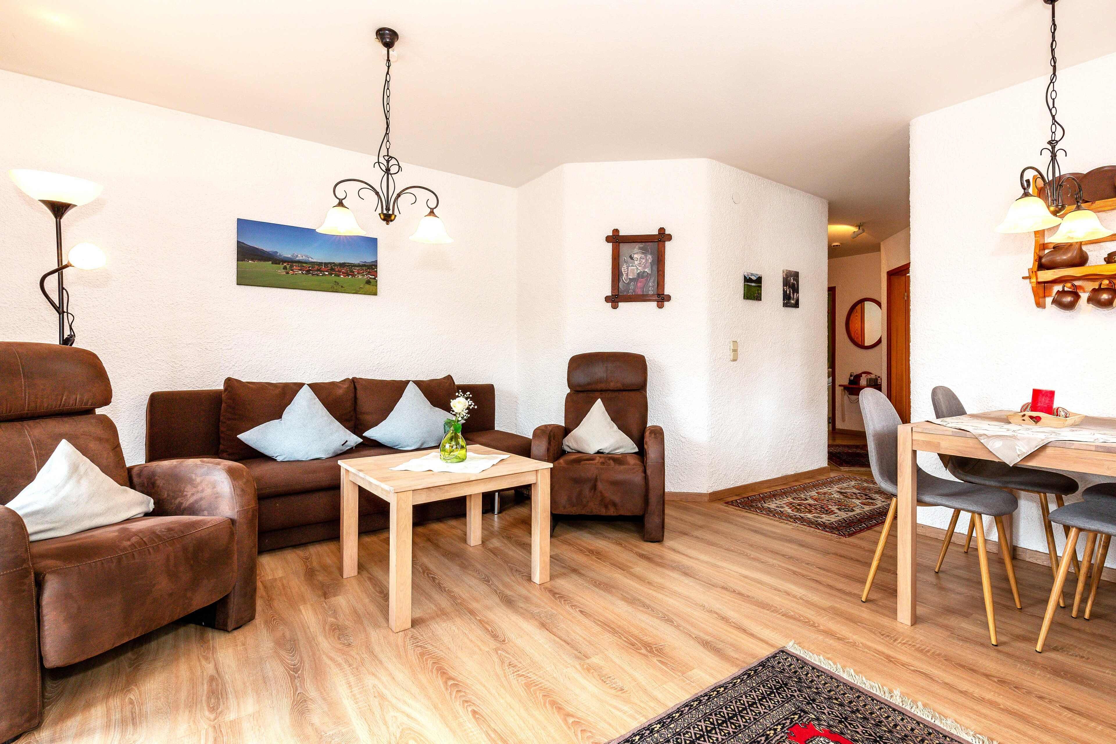A living room with a brown leather sofa, a wooden coffee table, and a dining area with a wooden table and chairs.