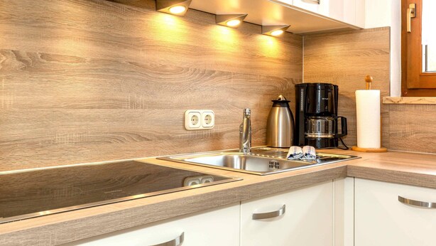 Une cuisine moderne avec un revêtement mural en bois, un évier en acier inoxydable et des armoires blanches.