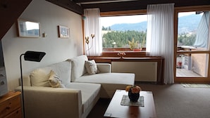 A cozy living room with a sofa, a table with a vase, a radiator, and a window with curtains. - Ferienwohnung Teddy, 68 m² (Siegsdorf)