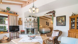 A cozy living room with a wooden table, wicker furniture, a television, and a fireplace. - Ferienwohnung 1, 65 qm, f. 1-2 Personen (Grassau)