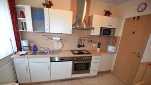 Cocina compacta con armarios blancos, una campana extractora de acero inoxidable, un microondas y un lavavajillas.