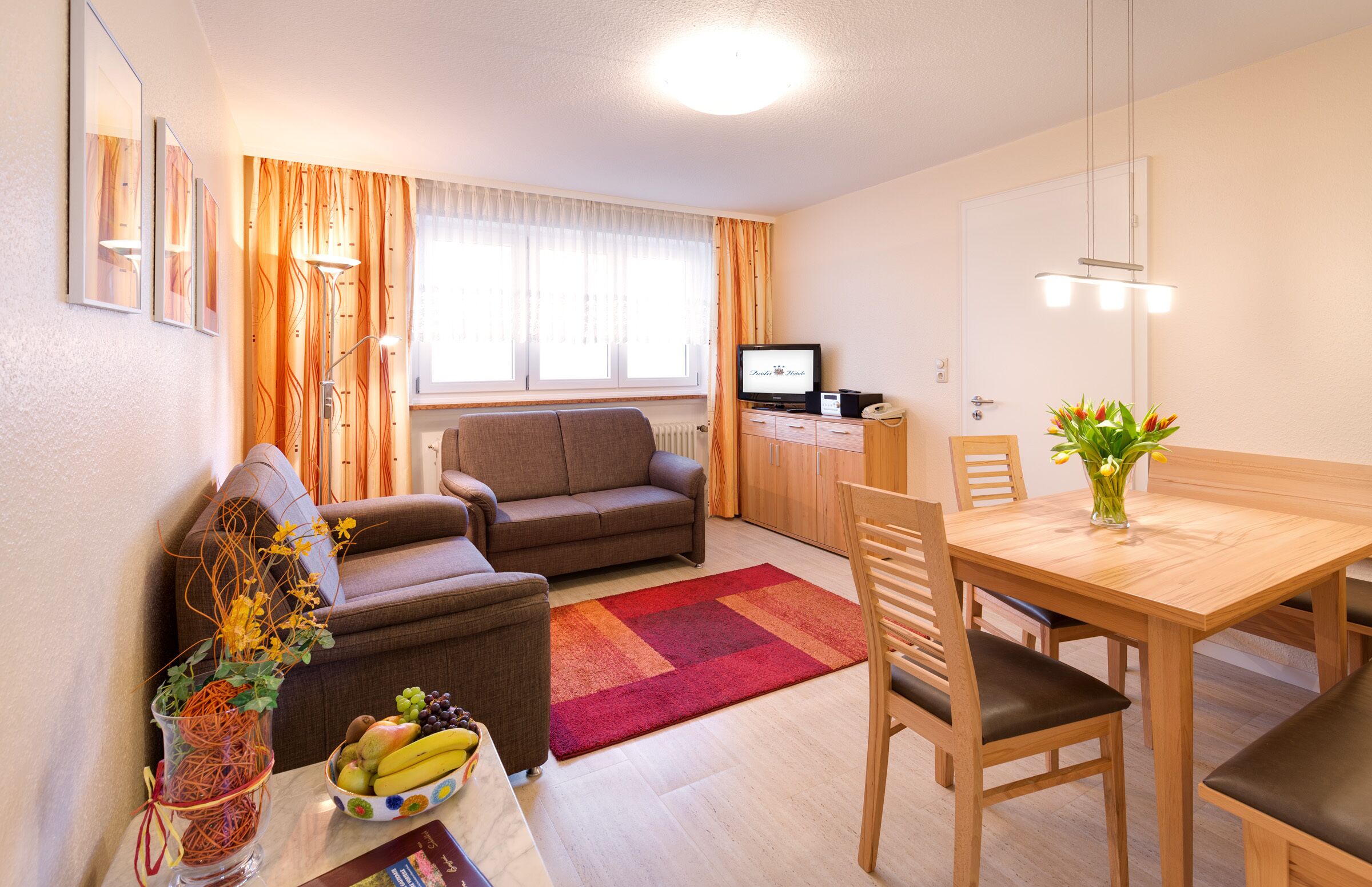Un salon moderne avec un canapé, une table à manger et des chaises, un téléviseur et un vase rempli de fleurs.
