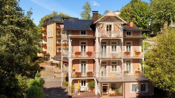 A multi-story hotel with balconies, outdoor seating, and a garden area.