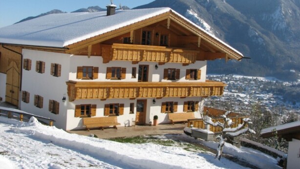 Een chalet met meerdere verdiepingen, houten balkons, een met sneeuw bedekte dak en een bergachtige achtergrond.