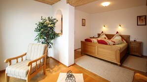 Een gezellige kamer met een houten plafond, een bed met rode en witte beddengoed, een houten stoel en een kamerplant.