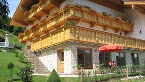 Een traditioneel gebouw in Alpenstijl met houten balkons versierd met bloemen, stenen muren en een stenen trap naar de ingang.