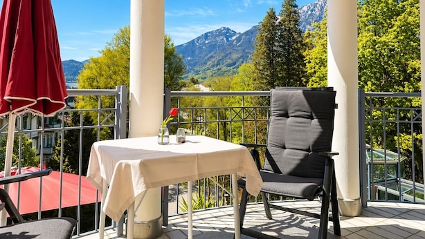 Uma varanda com mesa, cadeiras e um guarda-sol vermelho.