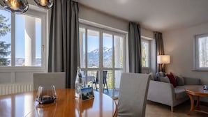 Quarto de hotel com uma mesa de jantar, cadeiras, um sofá e uma varanda com vista para as montanhas.