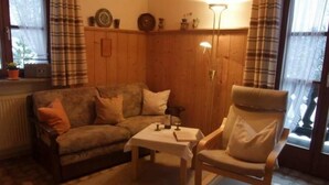 Un salón acogedor con un panel de madera, un sofá, un sillón y una mesita.