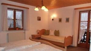 Una habitación acogedora con dos camas individuales, cabecero de madera, mesita de noche, ventana con cortinas y un aplique de pared.