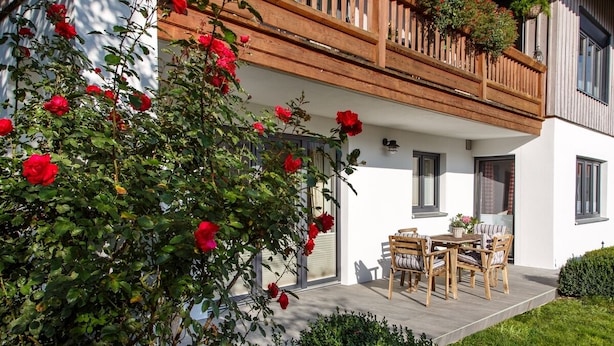 Et moderne hus med balkon, en have med røde roser og en terrasse med havemøbler.