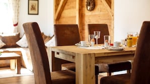 Et træbord dækket med klare glas, tallerkener og et kande appelsinjuice i et hyggeligt rum med trævægge og en hængende lampe.