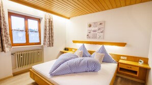 Um quarto com cama de madeira, mesa de cabeceira, cortinas numa janela, radiador e um quadro na parede.