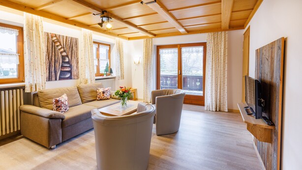 Uma sala de estar com sofá, duas poltronas, uma mesa de centro e uma TV sobre uma estante de madeira.