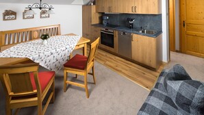 A compact kitchen with wooden cabinets, a countertop, and a dining area with a table and chairs. - Ferienwohnung 1 für 2 bis 4 Personen, 75 qm, 2 Schlafzimmer, Balkon (Schönau am Königssee)