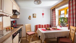A kitchen with wooden cabinets, a dining table with chairs, and a window with curtains. - Ferienwohnung 1 für 2 bis 4 Personen, 75 qm, 2 Schlafzimmer, Balkon (Schönau am Königssee)