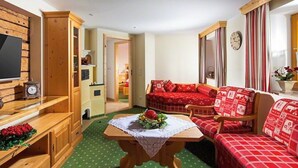 A cozy room with a wooden TV stand, a red sofa set, a small table with a floral centerpiece, and a green patterned carpet. - Ferienwohnung 1 für 2 bis 4 Personen, 75 qm, 2 Schlafzimmer, Balkon (Schönau am Königssee)