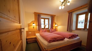 A wooden-framed bed with checkered bedding, two bedside lamps, and a window with curtains. - Ferienwohnung 1 für 2 bis 4 Personen, 75 qm, 2 Schlafzimmer, Balkon (Schönau am Königssee)