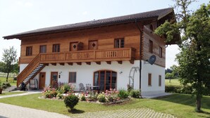 A two-story wooden house with a balcony, a staircase, and a garden with flowers. - Ferienwohnung "Chiemsee", 110 qm Erdgeschoss, 3 separate Schlafzimmer (Höslwang)