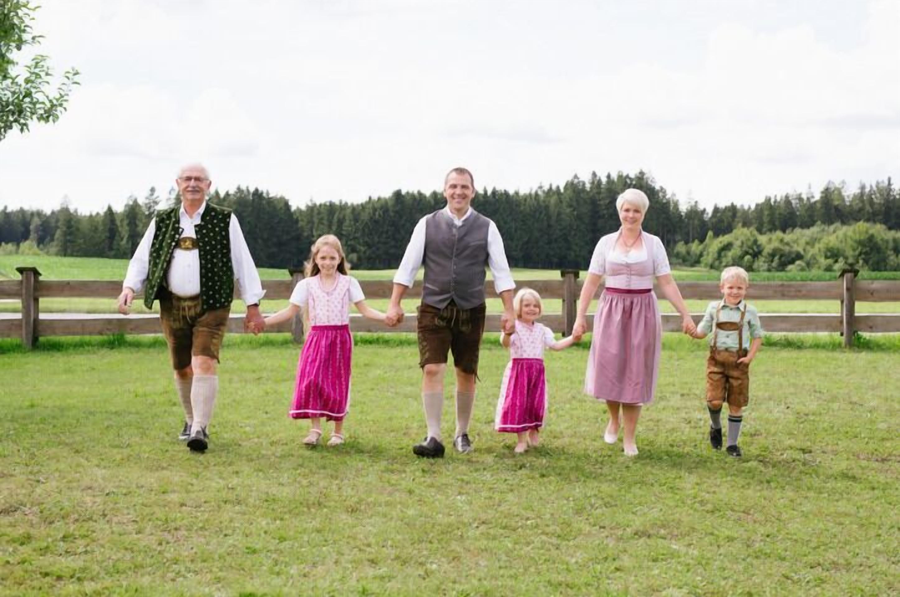 A family walking on a grassy field with a wooden fence and trees in the background.