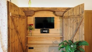 A rustic wooden TV stand with a flat-screen TV, a small shelf with a vase of flowers, and a potted plant. - Ferienwohnung "Chiemsee", 110 qm Erdgeschoss, 3 separate Schlafzimmer (Höslwang)