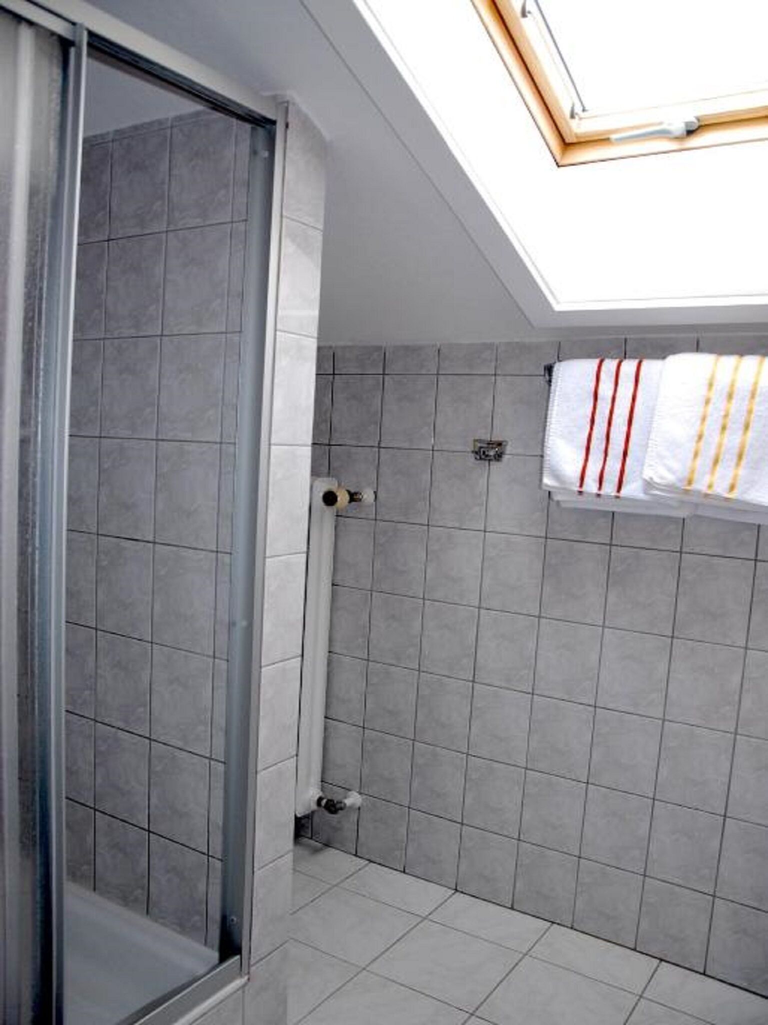 Un bagno moderno con piastrelle grigie, cabina doccia in vetro e un lucernario sopra la doccia.