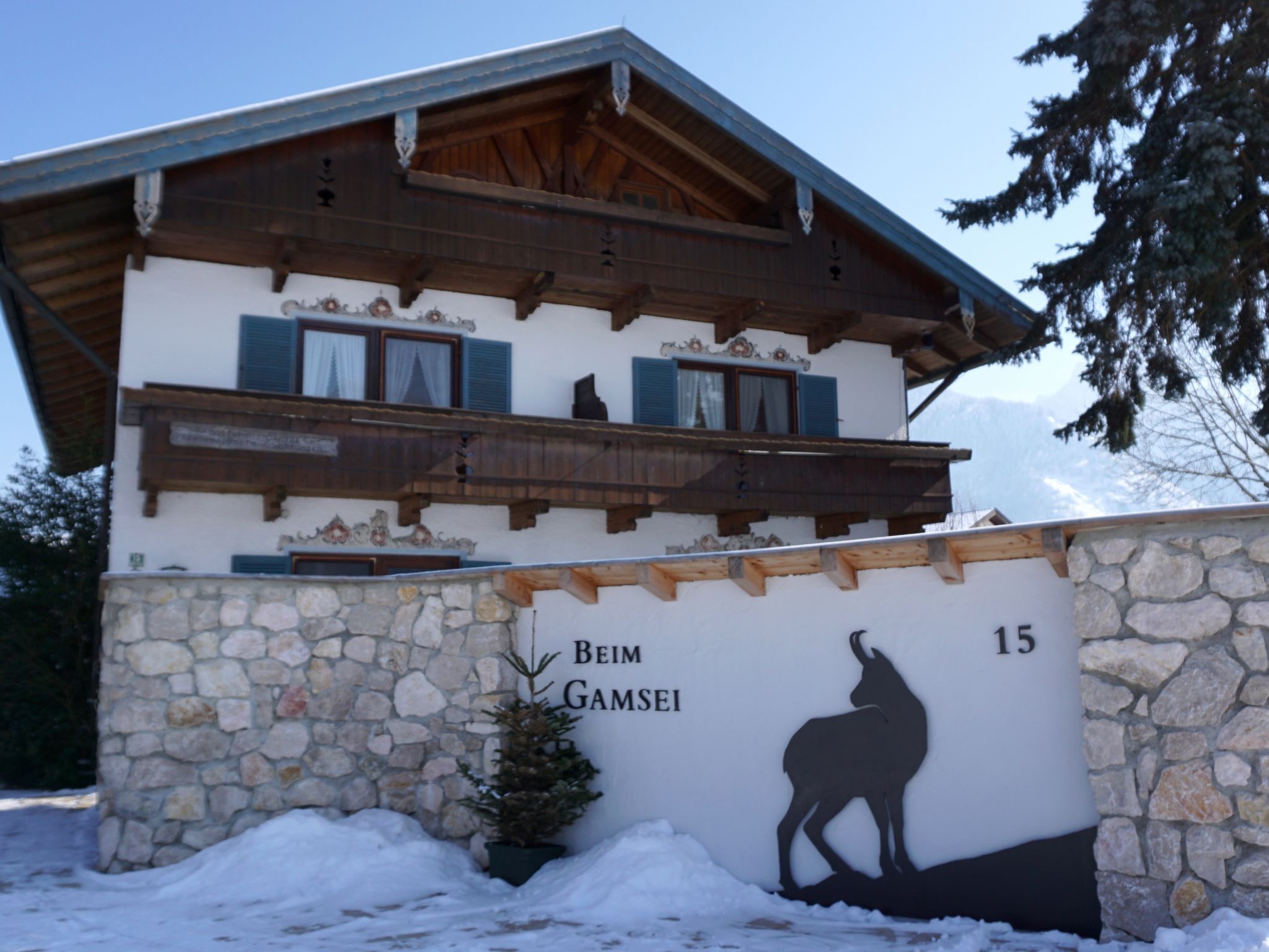 A two-story building with a stone facade and a wooden balcony. The building has a sign with a silhouette of a horse and the text 'Beim Gamsei 15'.
