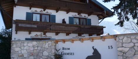 A two-story building with a stone facade and a wooden balcony. The building has a sign with a silhouette of a horse and the text 'Beim Gamsei 15'.