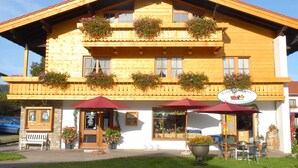 Um edifício de madeira tradicional com varandas decoradas com flores, mesas ao ar livre e uma placa indicando um café.