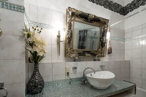 Ein Badezimmer mit einem weißen Waschbecken, einem großen, verzierten Spiegel und einer Vase mit weißen Blumen auf der Ablagefläche.