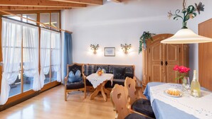A cozy room with a wooden ceiling, a sofa, a dining table with a white tablecloth, and a chandelier. - Three-room vacation apartment 65sqm, shower/WC, 2 extra bedrooms, kitchen, balcony (Reit im Winkl)