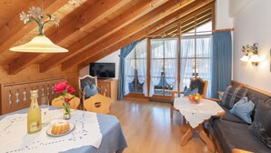 A cozy, wooden-floored room with a dining table set for two, a sofa, and a television. - Three-room vacation apartment 65sqm, shower/WC, 2 extra bedrooms, kitchen, balcony (Reit im Winkl)