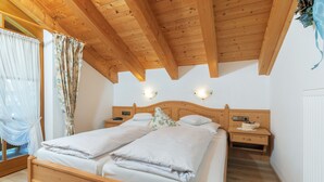 A double bed with white linens, wooden headboard, bedside tables with lamps, and a window with curtains. - Three-room vacation apartment 65sqm, shower/WC, 2 extra bedrooms, kitchen, balcony (Reit im Winkl)