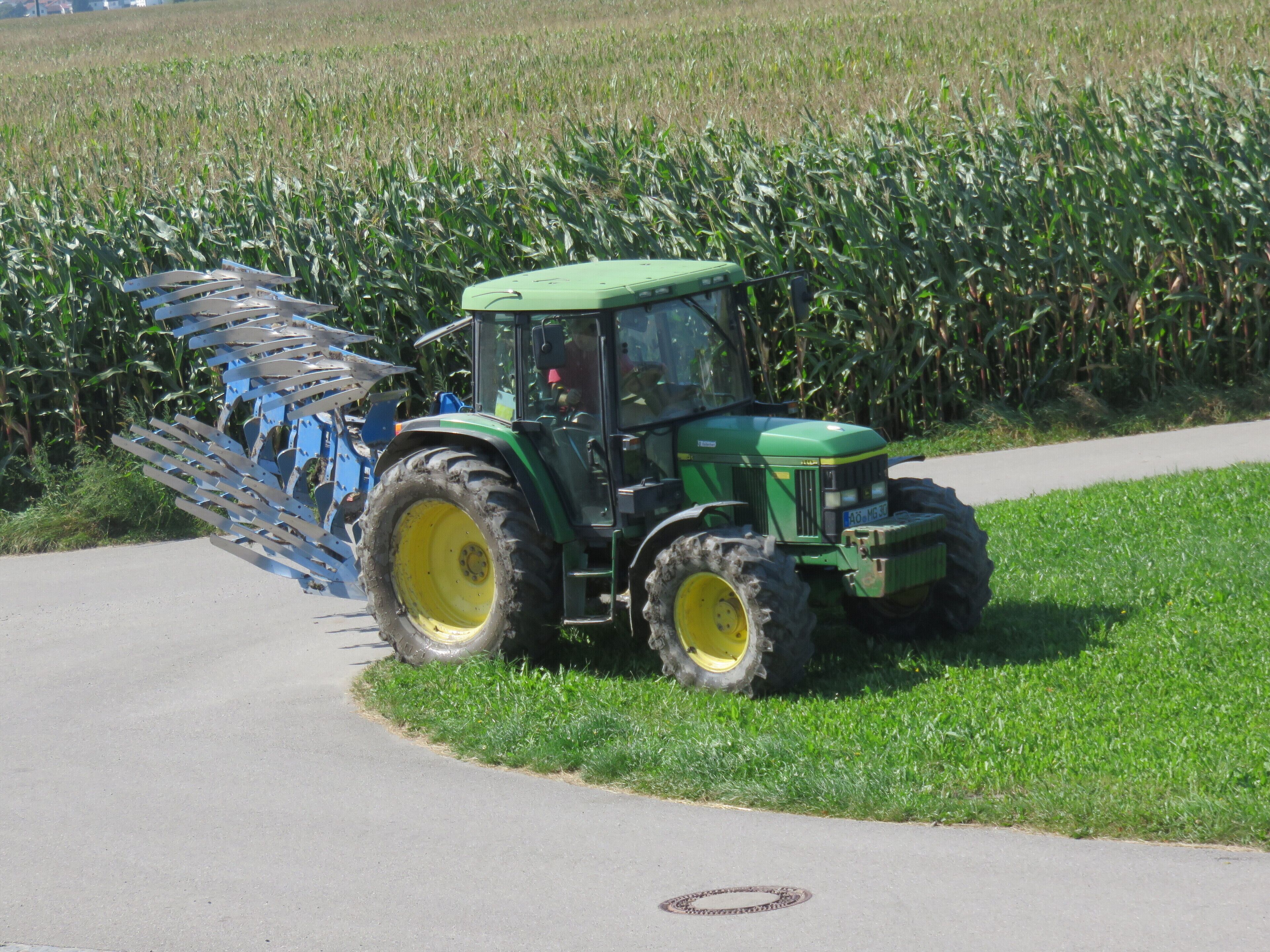 Un tracteur vert avec un accessoire bleu, dans un champ.