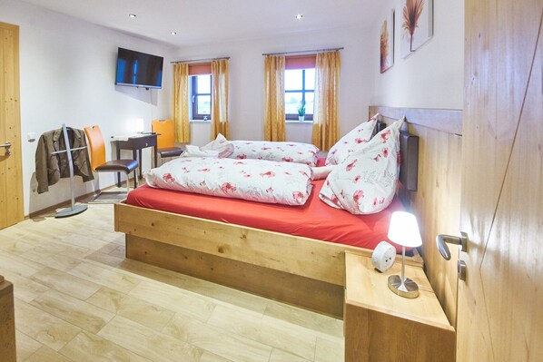 A bedroom with a wooden bed, a desk, a chair, a TV, and two windows with curtains. - Apartment Oberstadel 52 sqm for 1-4 persons barrier-free (Altötting)