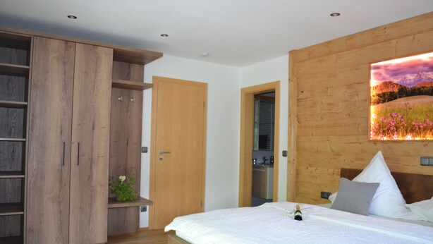 A bedroom with a wooden wardrobe, a bed with pillows, and a wall-mounted picture.