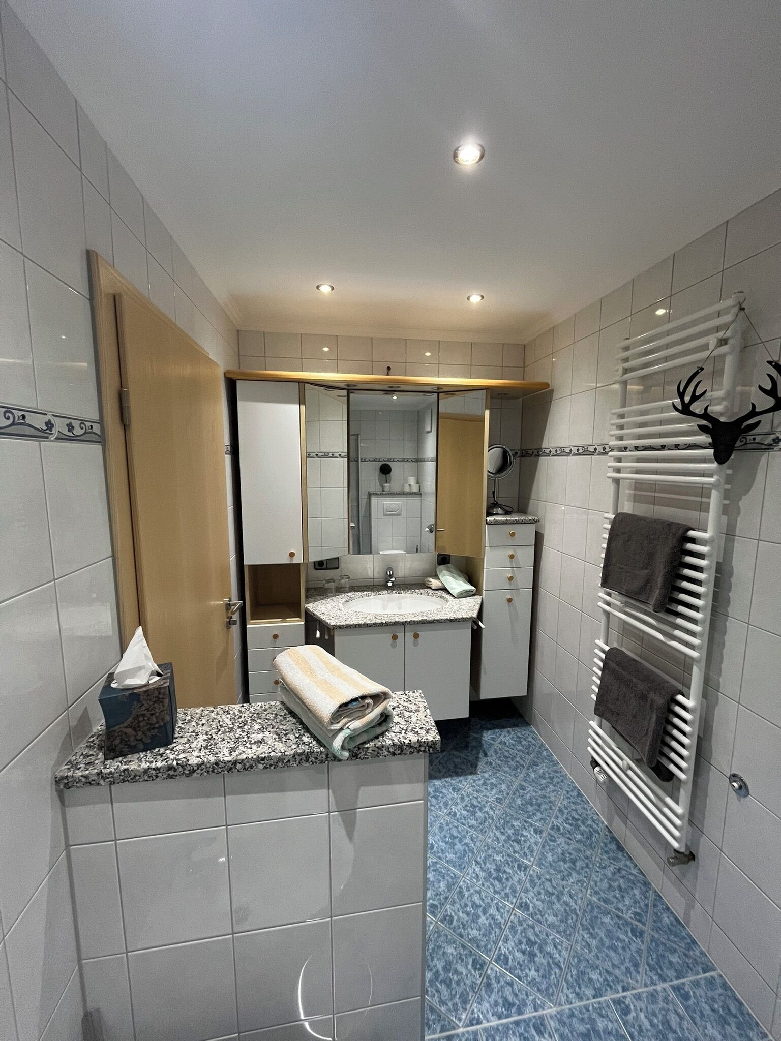 A bathroom with white tiles, a sink, a mirror, and a towel rack with towels.