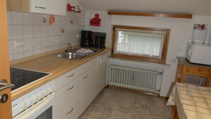 Une petite cuisine équipée d’une cuisinière, d’un évier et d’une fenêtre avec des rideaux.