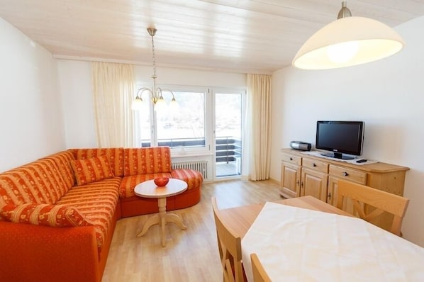 A cozy room with a sofa, a small round table, a TV on a wooden cabinet, and a window with curtains.